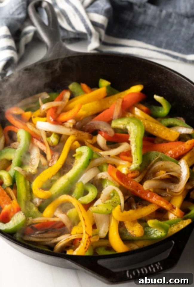 Sliced peppers and onions being sauteed in skillet. 