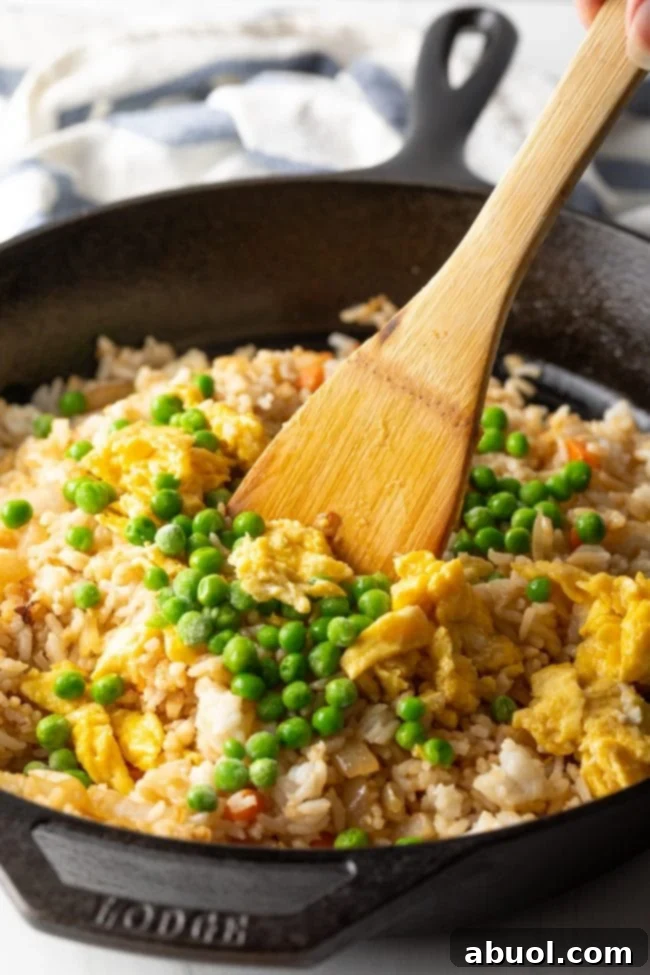 A spatula combining cooked rice and vegetables in a skillet, ensuring even coating.