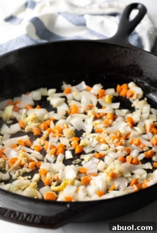 Chopped vegetables, including onions and carrots, being sautéed in a skillet.