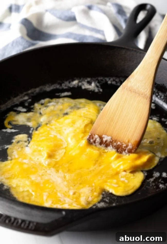 Eggs being scrambled in a pan, forming fluffy curds.