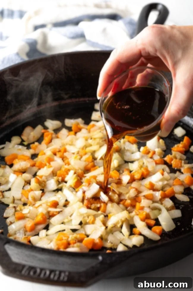 A hand pouring a stir-fry sauce mixture over sautéed vegetables in a pan.