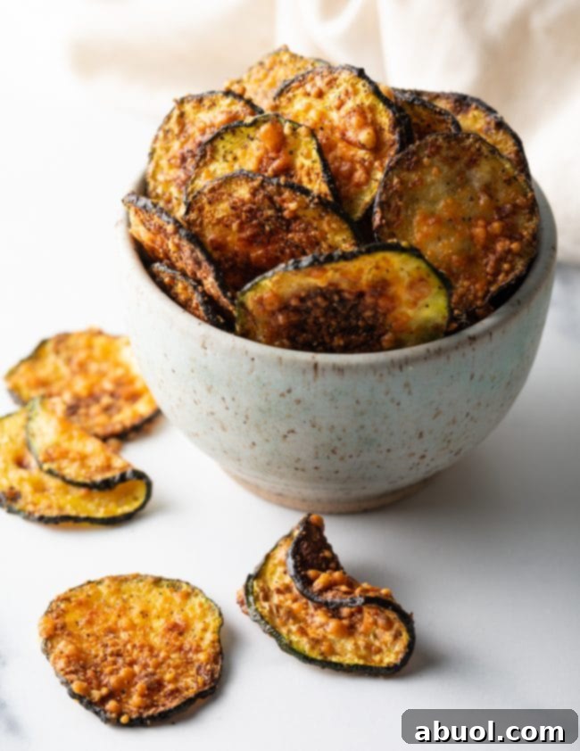 Crispy Air Fryer Zucchini Crisps 3 Full view of speckled bowl overflowing with parmesan zucchini crisps and chips scattered around.