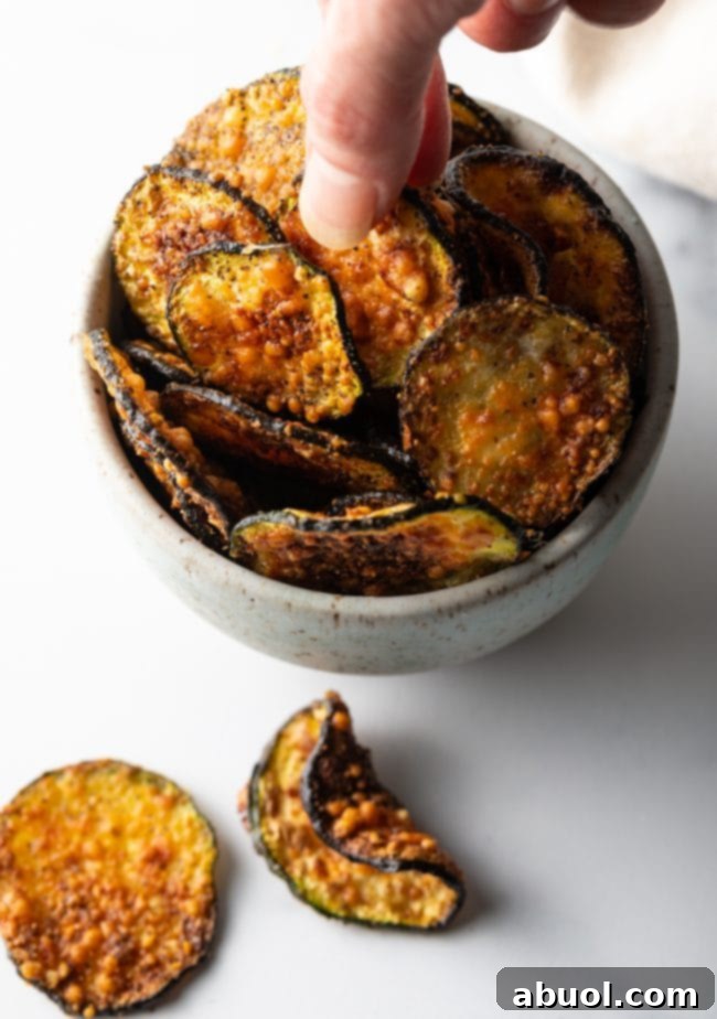 Crispy Air Fryer Zucchini Crisps 4 Top down view of hand grabbing a chip from a bowl filled with chips.