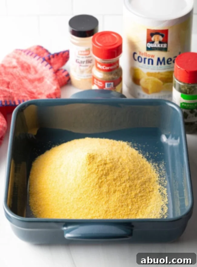 A square baking pan filled with golden yellow cornmeal, ready for the fish coating. The texture is coarse and inviting, promising a crispy crust.