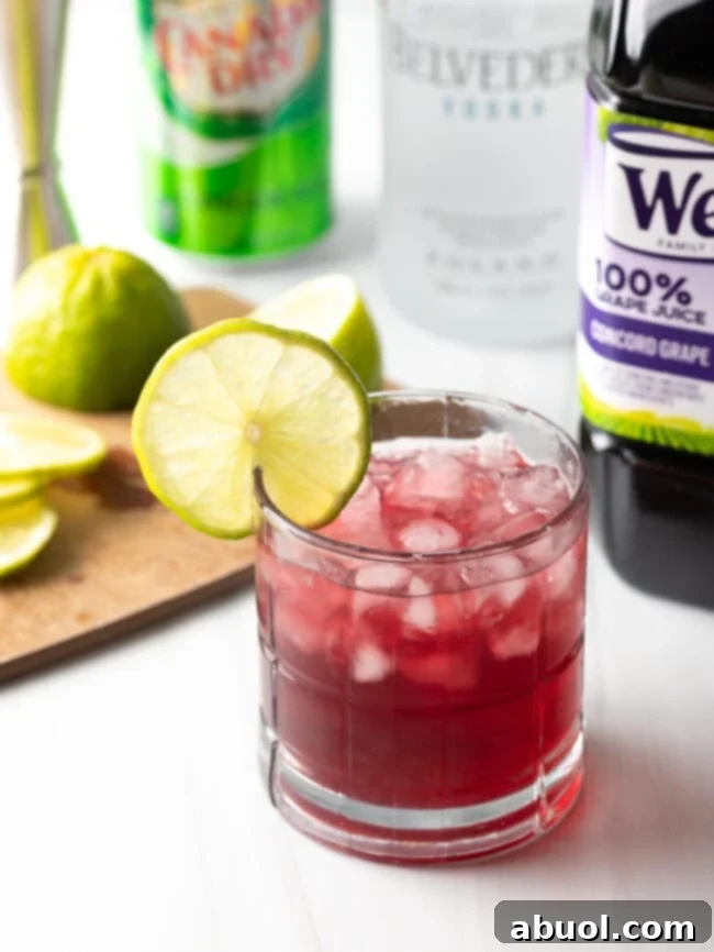 Full shot of a freshly prepared transfusion drink, garnished with a lime wedge, with ingredients subtly blurred in the background.