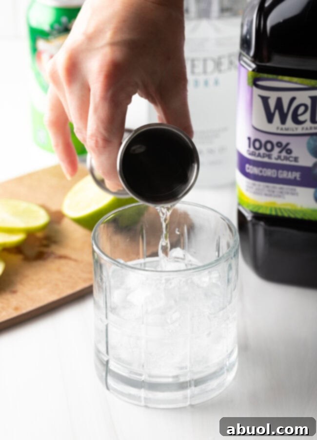 Hand adding a measured amount of vodka from a jigger to a glass filled with ice.