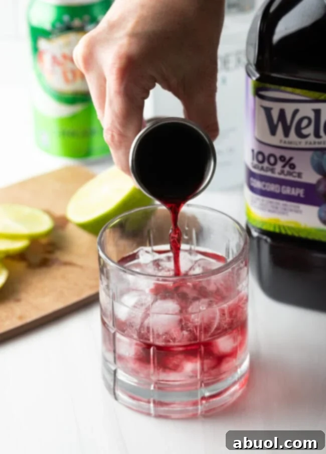 Hand pouring grape juice into a tumbler with ice and other liquids.