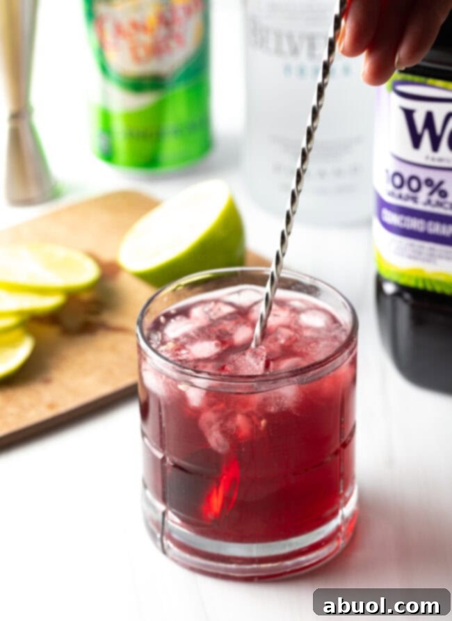 Metal swizzle stick stirring a transfusion cocktail in a glass, showing the blend of colors.