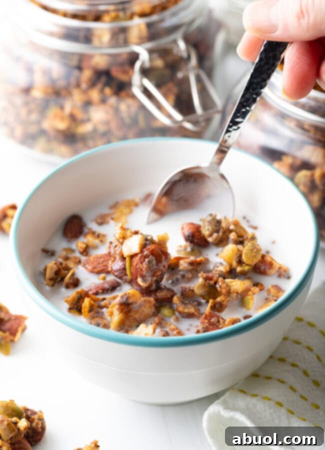 Ultimate Keto Granola Crunch 4 Bowl with keto granola and milk, hand scooping with spoon.