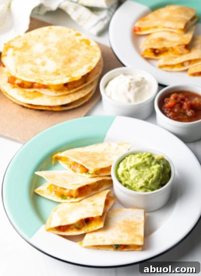 Full spread of shrimp quesadillas on plates, stacked in background, ramekins of guacamole, sour cream, and salsa.