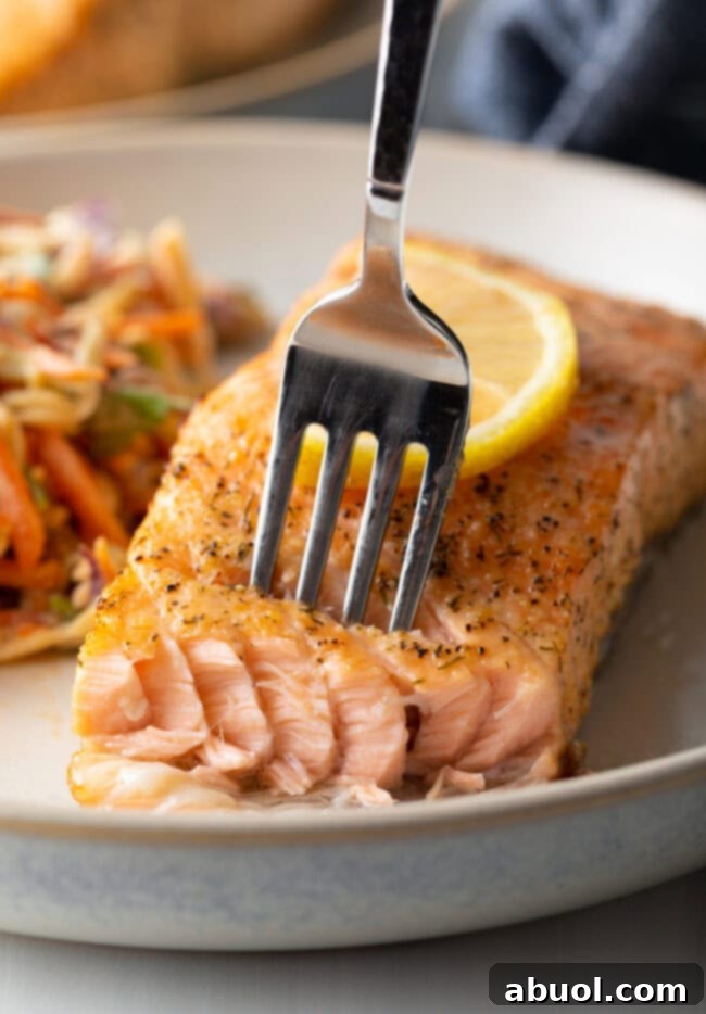 A fork taking a delicious bite of air-fried salmon, highlighting its flaky texture.