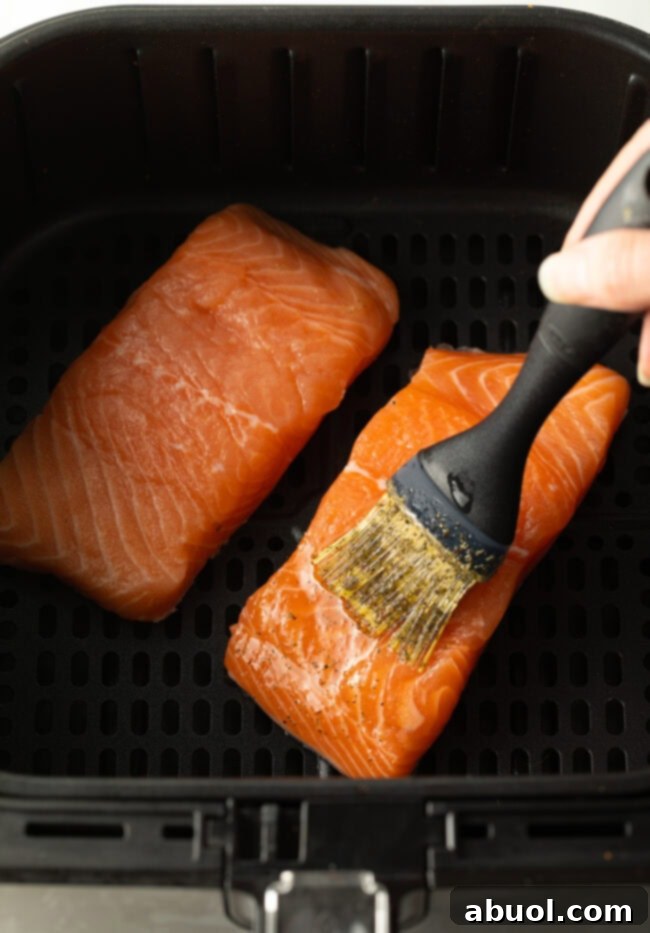 A hand brushing the delicious seasoning blend over the uncooked salmon fillets.