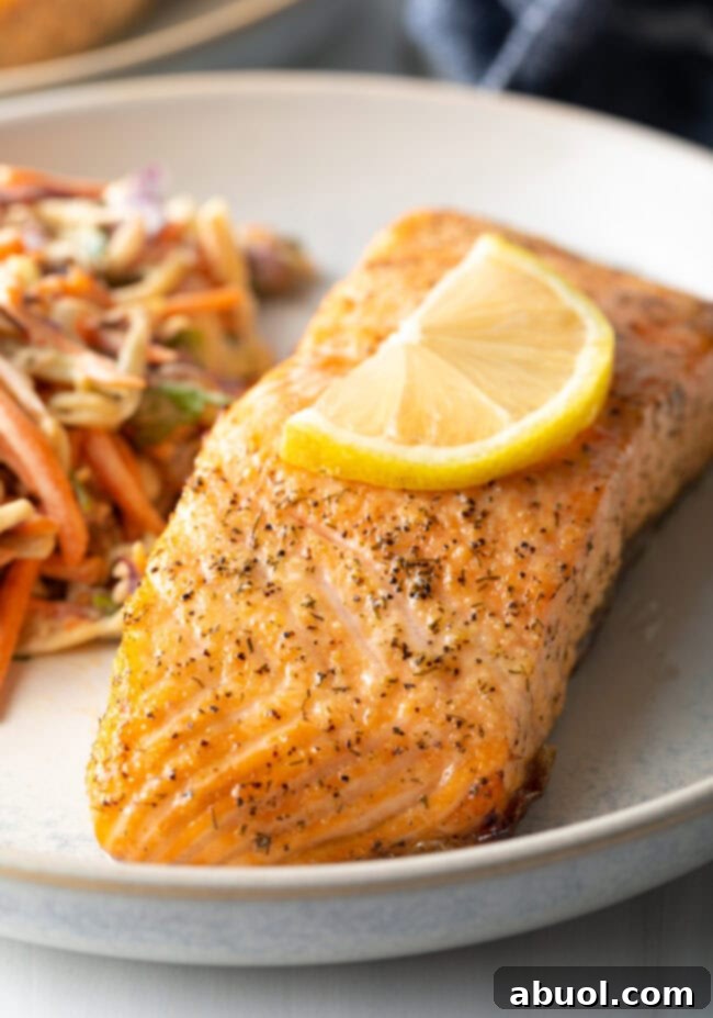 Close-up view of a perfectly cooked salmon fillet on a plate, garnished with a lemon slice and a side of coleslaw.