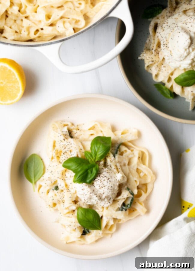 Top-down view of a bowl of lemon ricotta pasta, with the cooking pan of pasta visible in the background.