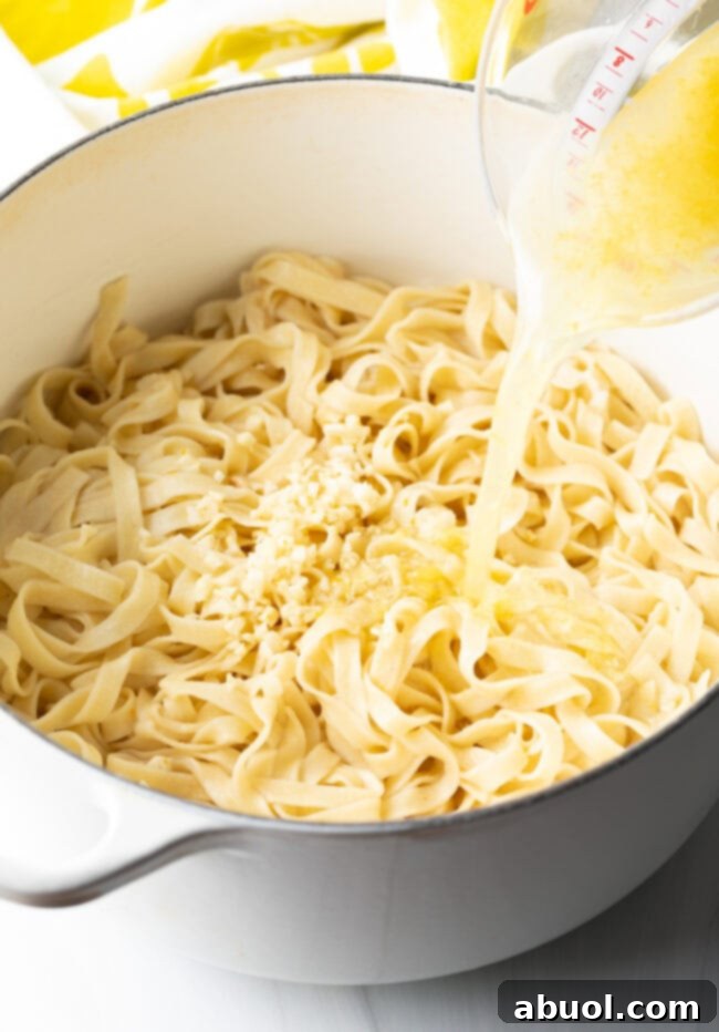 Adding fresh lemon juice, water, and minced garlic to the pot of fettuccine noodles, stirring to combine.