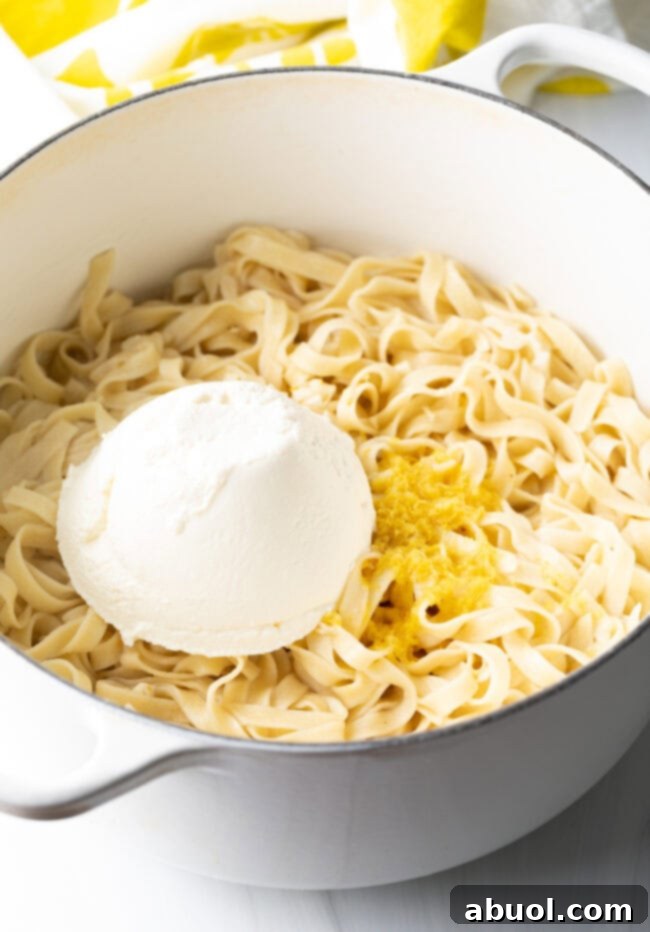 A large scoop of ricotta cheese being added to the pot of fettuccine with garlic and lemon.