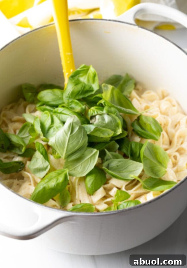 Fresh basil being stirred into the pot of lemon ricotta pasta.