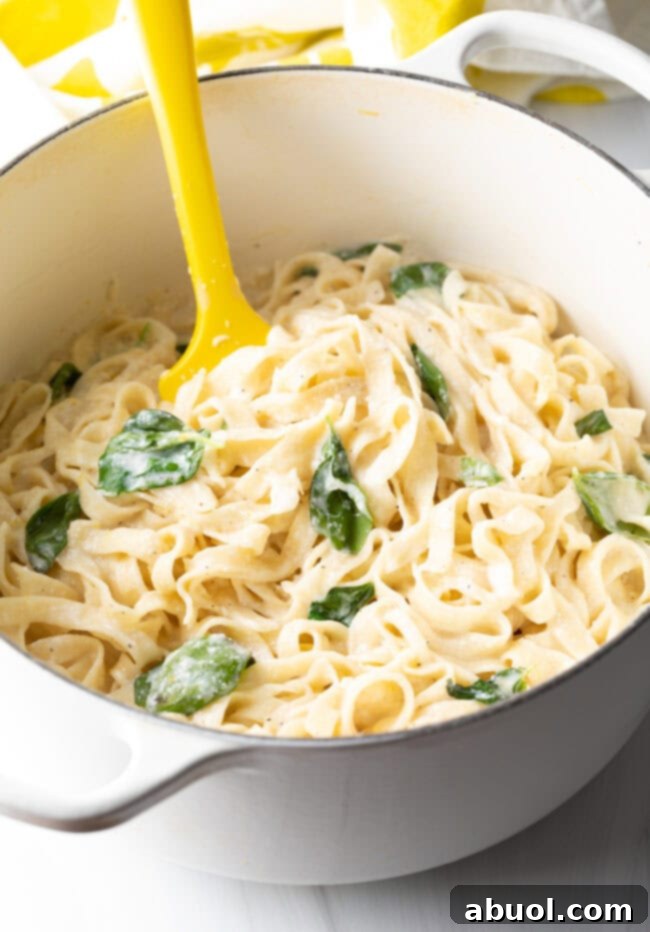 Close-up of fettuccine noodles in a pot, coated in a creamy lemon cheese sauce and flecked with fresh basil.