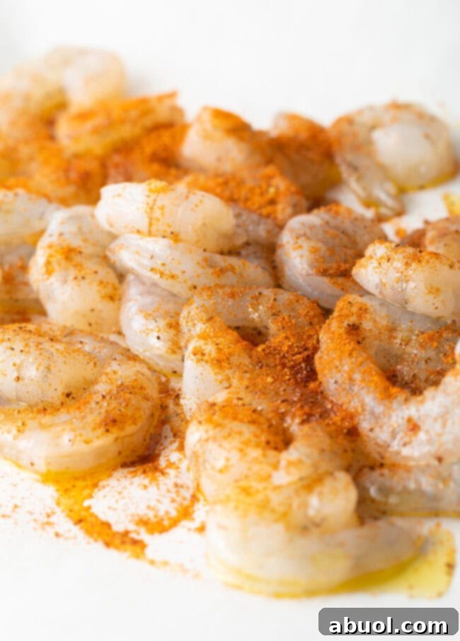 Raw shrimp tossed thoroughly with a generous amount of vibrant Cajun seasonings in a mixing bowl.