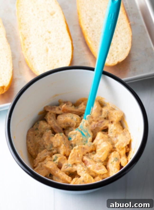 Shrimp bread filling ingredients, including cooked shrimp, mayonnaise, lemon zest, and parsley, perfectly combined in a bowl with a blue spatula.