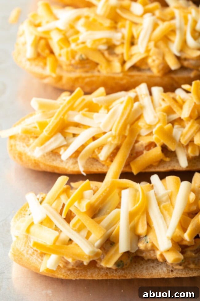 Generous layer of shredded cheddar and Monterey Jack cheese scattered over the shrimp mixture on the baguette slices, ready for baking.