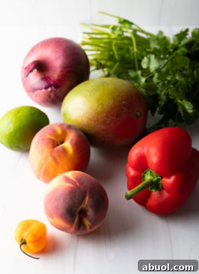 Ingredients laid out on a surface: fresh mango, peaches, red bell peppers, habanero, lime, and red onion, ready for preparation.