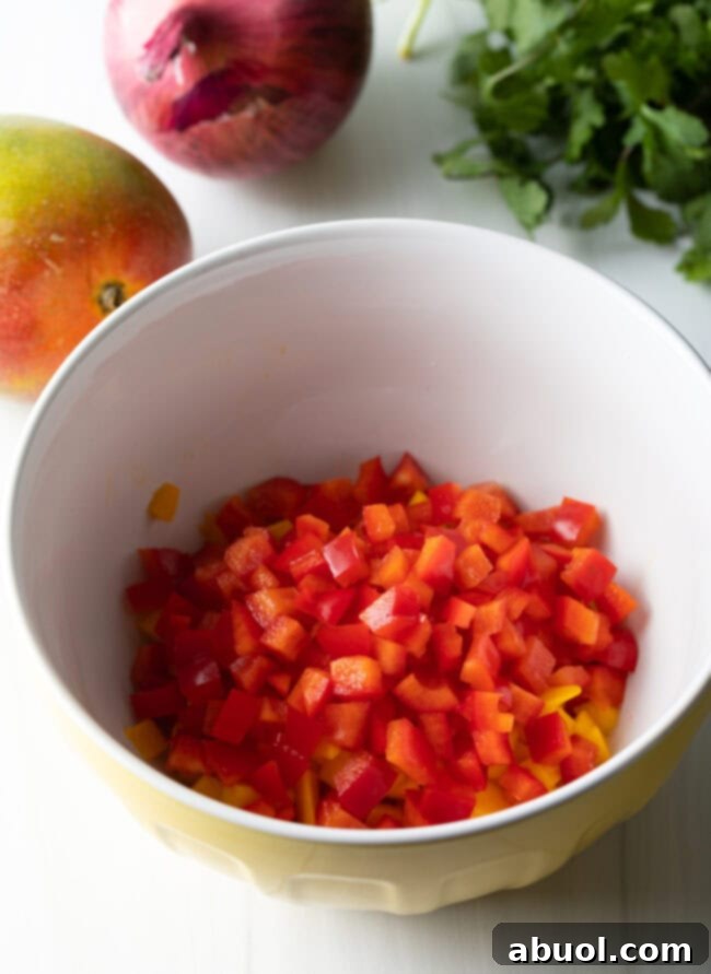 Diced red bell peppers being added to a bowl already containing other salsa ingredients.