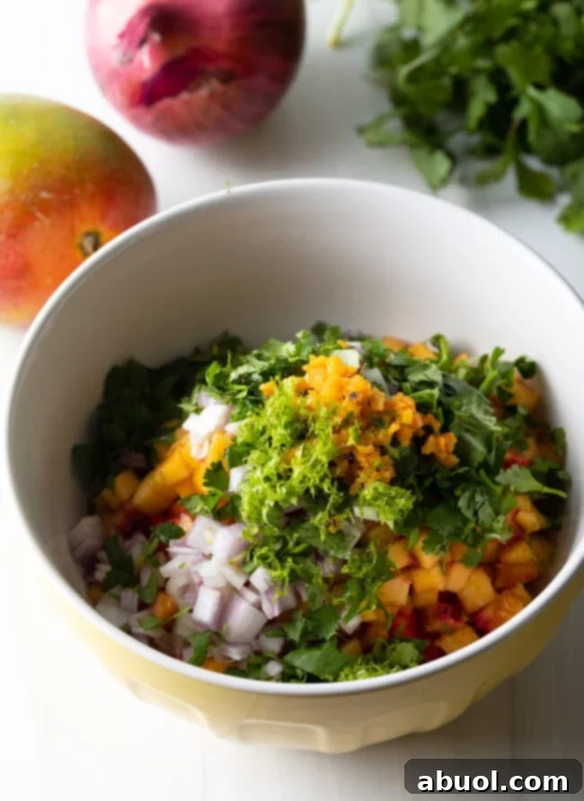 Lime zest, minced habanero, chopped cilantro, and diced red onion being added to the mixing bowl with fruits.