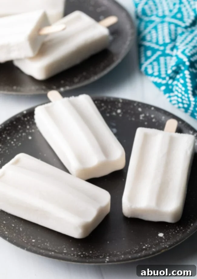 Three perfectly frozen coconut milk popsicles presented on a clean plate.