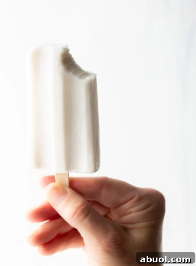 A hand holding a coconut milk popsicle with a bite taken out, showing the perfect frozen consistency.