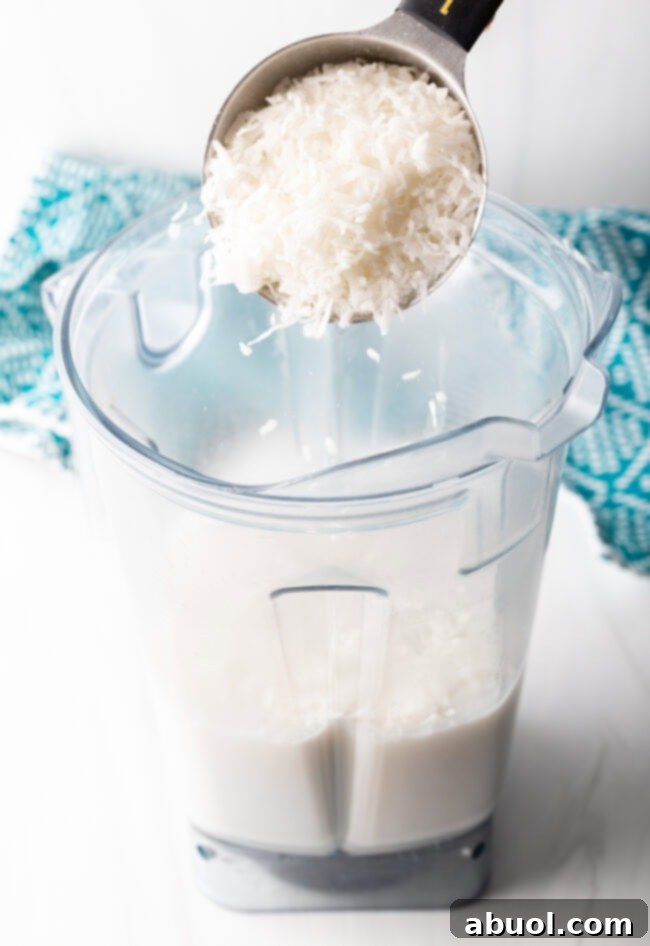 Adding shredded sweetened coconut to a blender with coconut milk, sugar, vanilla, and salt.
