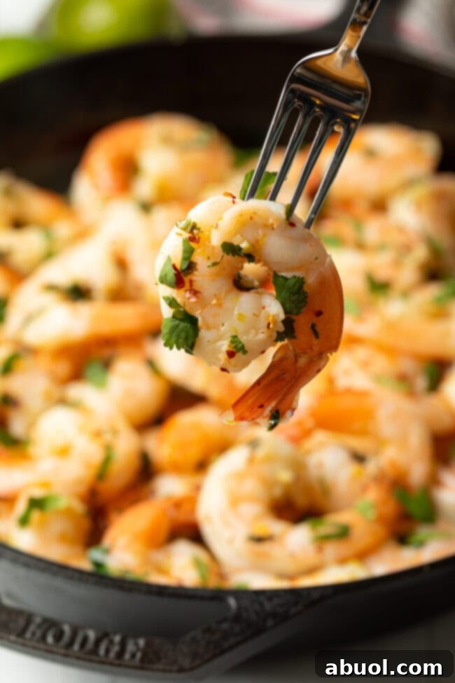 A fork holding a perfectly cooked tequila lime shrimp, showcasing its vibrant color and texture.