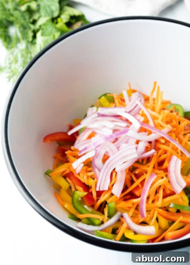 Colorful Pepper Medley 7 Sliced bell peppers, shredded carrots, and thinly sliced red onion uniformly cut and placed in a large mixing bowl, ready for the next step.