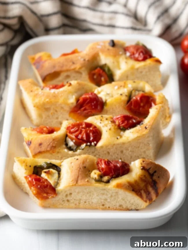 Slices of tomato basil focaccia bread on a white platter, showcasing its golden crust and vibrant toppings.