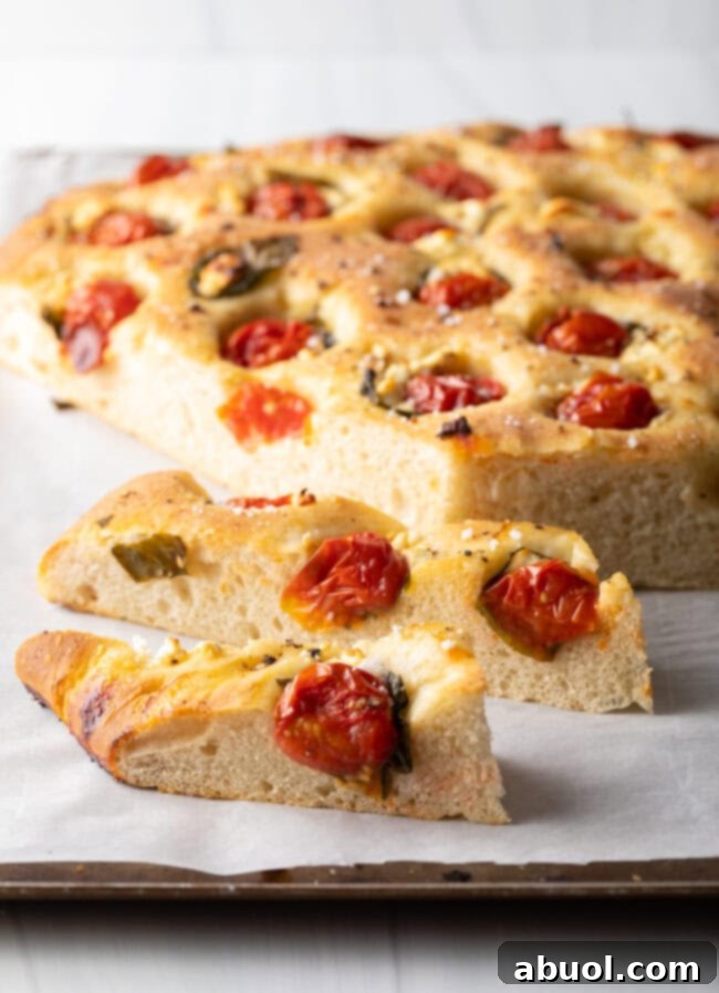 A large, golden-brown loaf of tomato basil focaccia bread, freshly baked and sliced, revealing its soft interior.