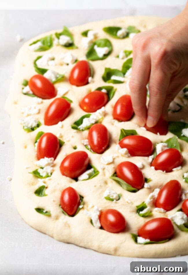 The fully topped focaccia dough, covered with tomatoes, basil, and goat cheese, ready for its second rise.