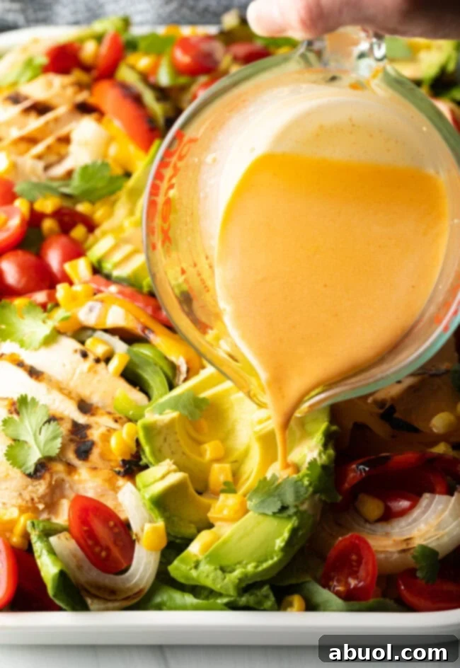Dressing being elegantly poured over the assembled chicken fajita salad.