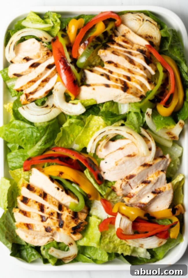 Overhead view of lettuce topped with sliced grilled chicken and colorful vegetables.