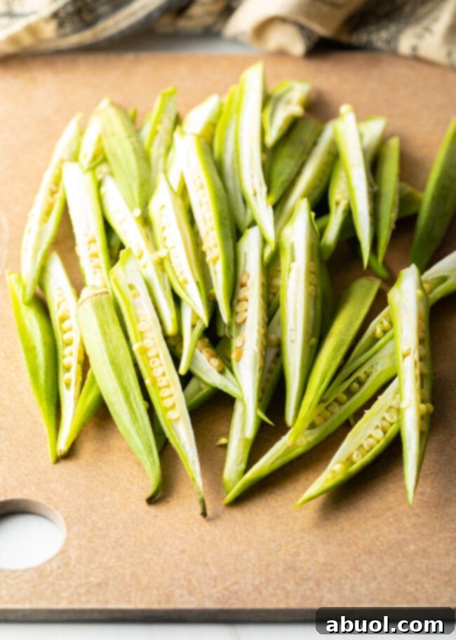 Raw fresh okra pods meticulously sliced lengthwise into quarters on a cutting board, creating fry-like pieces.