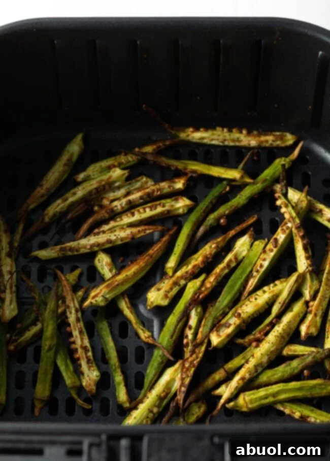 Thinly sliced okra pieces cooking and crisping up in an air fryer, nearly golden brown.