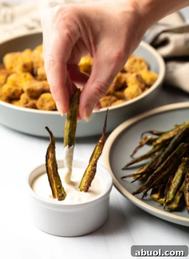 A hand gracefully dipping a crispy okra fry into a creamy aioli sauce, highlighting the perfect pairing.