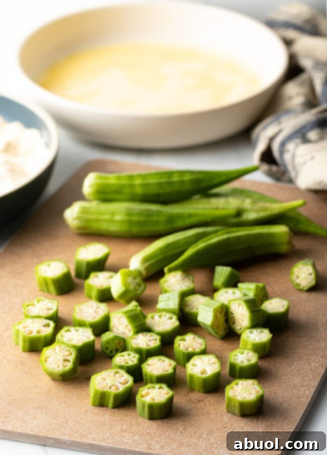 Fresh okra pods meticulously chopped into half-inch rounds on a wooden cutting board.