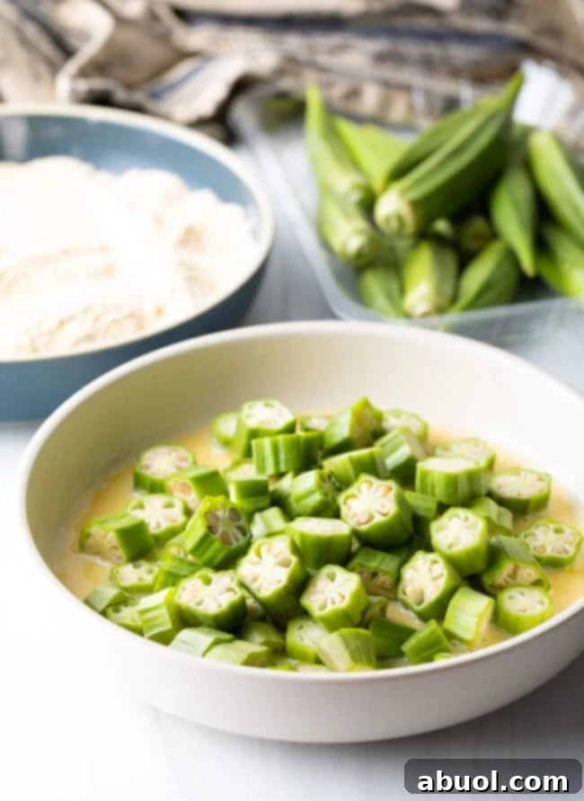 Raw, chopped okra pieces being tossed in an egg wash mixture in a bowl, preparing for breading.