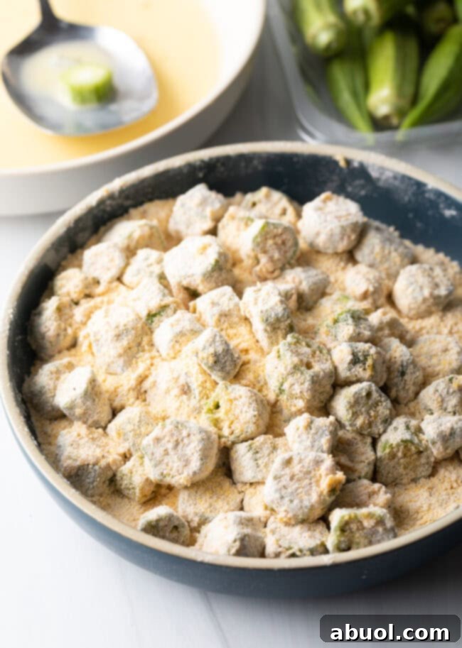 Uncooked okra slices generously coated in a cornmeal breading, ready for air frying.