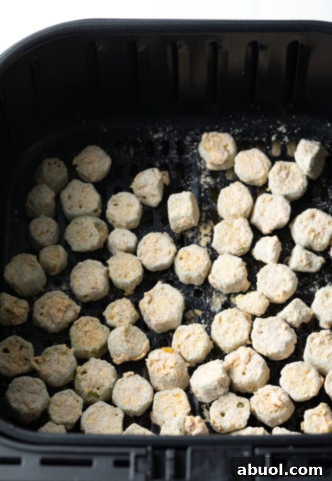 Lightly battered okra pieces arranged in a single layer within an air fryer basket, ready for cooking.
