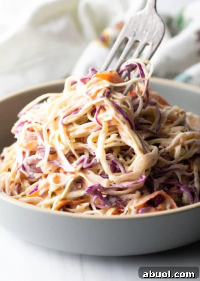 Fork taking bite from pile of creamy coleslaw, showcasing its rich texture.