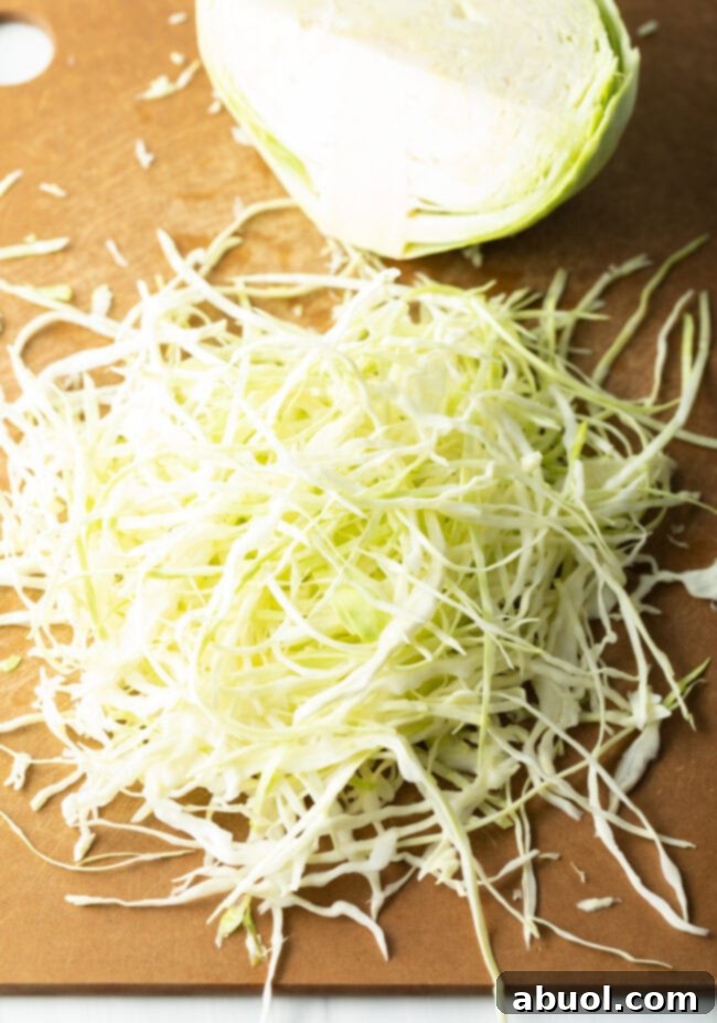 Freshly shredded green cabbage resting on a wooden cutting board, ready for mixing.