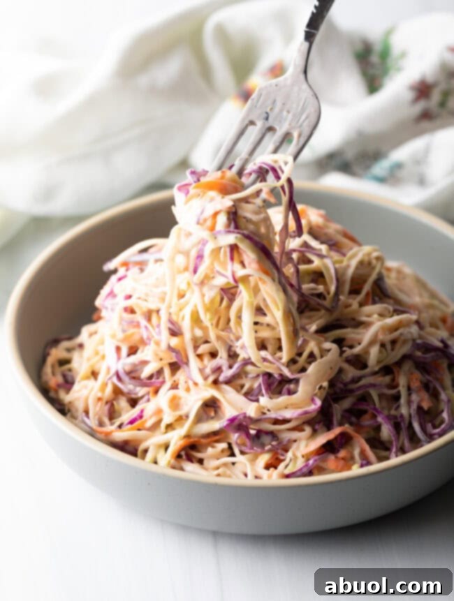 Fork taking a bite of creamy coleslaw from a bowl, highlighting its appetizing texture.