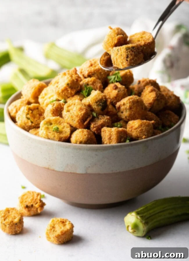 Spoon adding pieces of southern fried okra to a bowl.