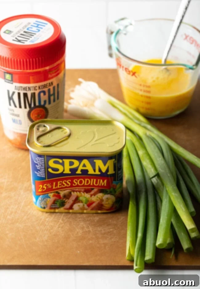 Ingredients on a cutting board: kimchi, can of spam, scrambled raw eggs, fresh green scallions.